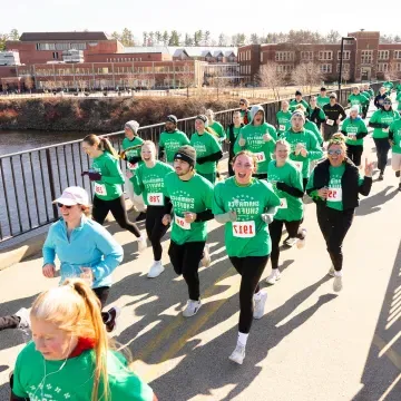 runners in green shirts crossing campus footbridge for a race 